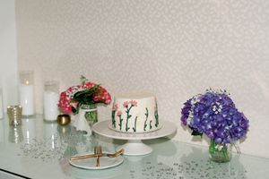Elegant cake display with floral decorations, white candles, and purple hydrangeas on a mirrored table.
