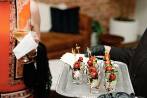 Server holding a silver tray of elegant caprese appetizer shots at an upscale catered wedding cocktail hour