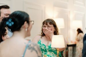 Woman in green floral dress covers her mouth in surprise at a wedding reception event.Documentary-Inspired wedding photography Wilmington NC