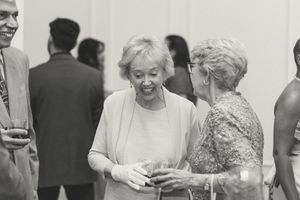 Black and white photo of elderly women socializing at a formal event, smiling and holding drinks. Documentary-Inspired wedding photography