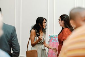 Two women smiling and conversing at a networking event, one holding a colorful gift bag. Documentary-Inspired wedding photography Wilmington