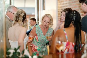Guests mingling at a wedding reception, holding wine glasses, wearing colorful attire in a brick-walled venue.