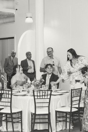 Black and white wedding reception photo of guests toasting the bride and bride seated at an elegant table. Documentary-Inspired weddings