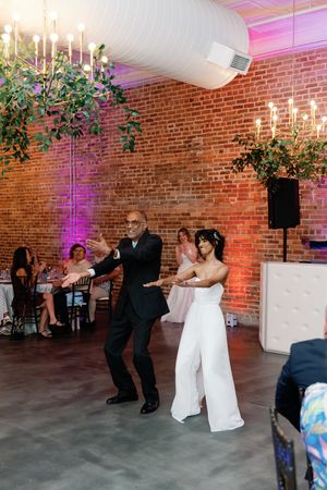 Bride in white jumpsuit dances with father in black suit at her wedding. Wilmington NC Wedding Photography