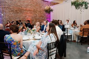 Guests seated at round tables during a wedding reception in a rustic brick venue with warm ambient lighting. The Elia