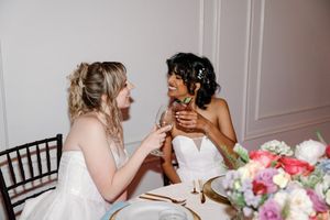 Two brides sharing a joyful moment at their wedding reception table with colorful floral arrangements. NC Weddings