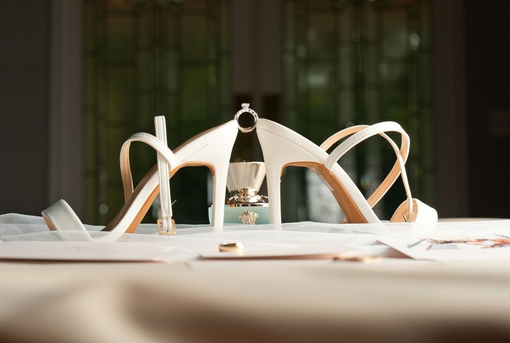 Elegant white strappy heeled sandals displayed on a table with a ring tucked inside, captured in soft natural light.