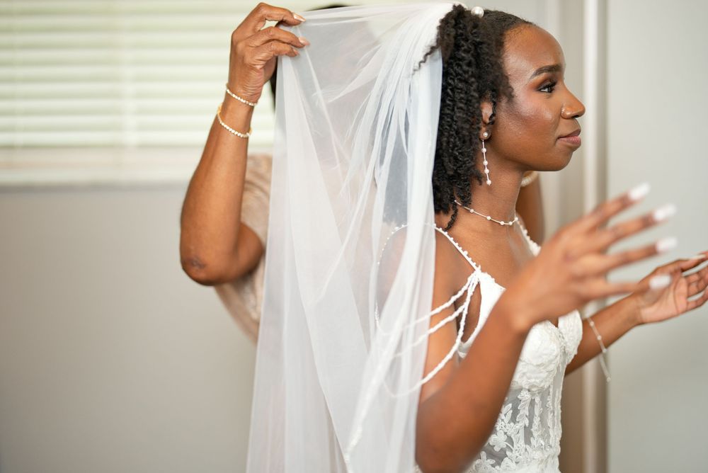 Bride in lace gown and white veil being prepared for wedding ceremony by bridesmaid.