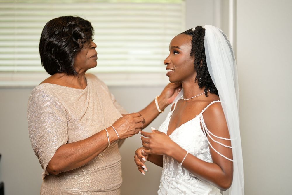 A mother lovingly adjusts her daughters necklace as the Black bride prepares in her white wedding dress and veil.
