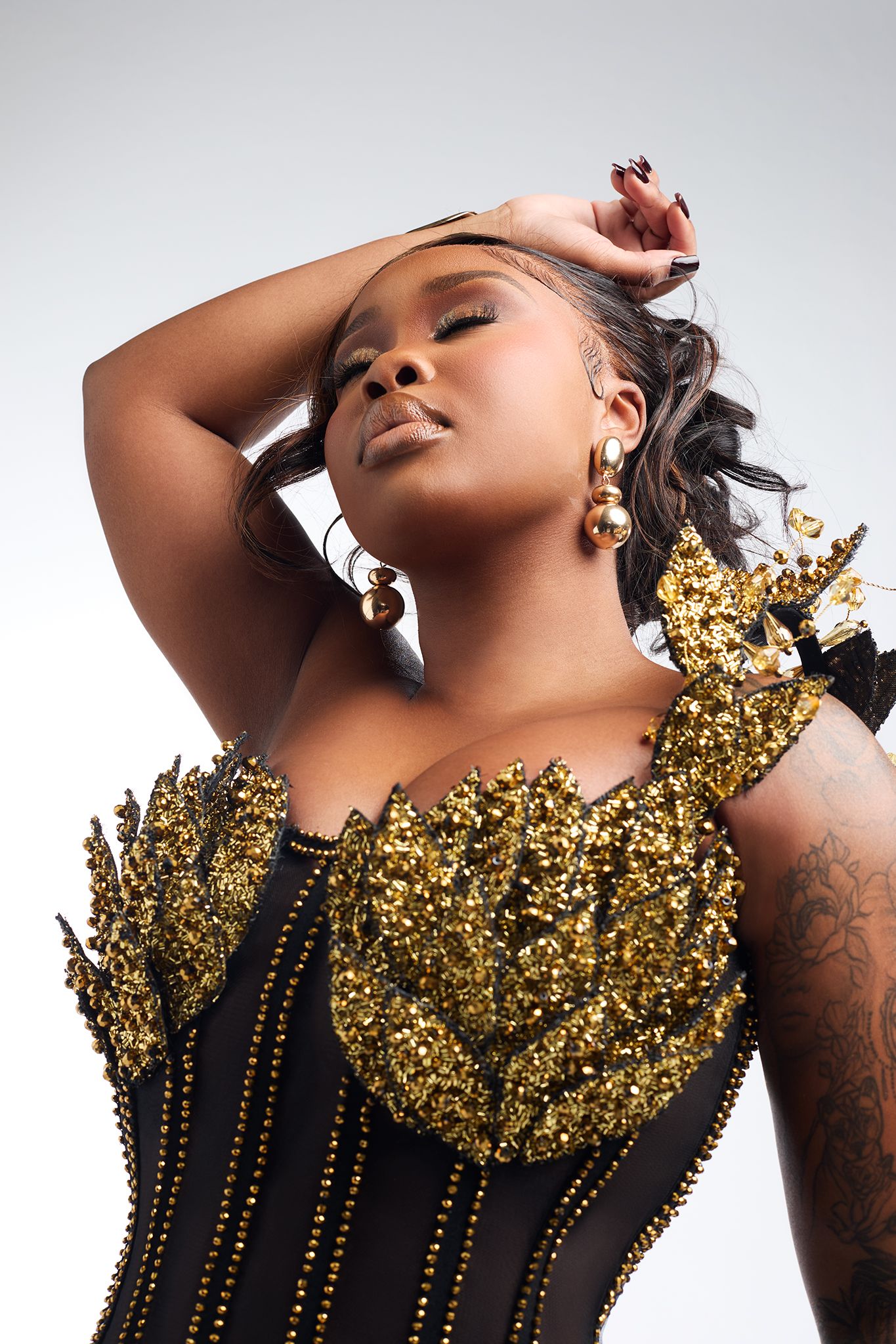 Woman in black and gold sequined corset top posing with hand in hair.