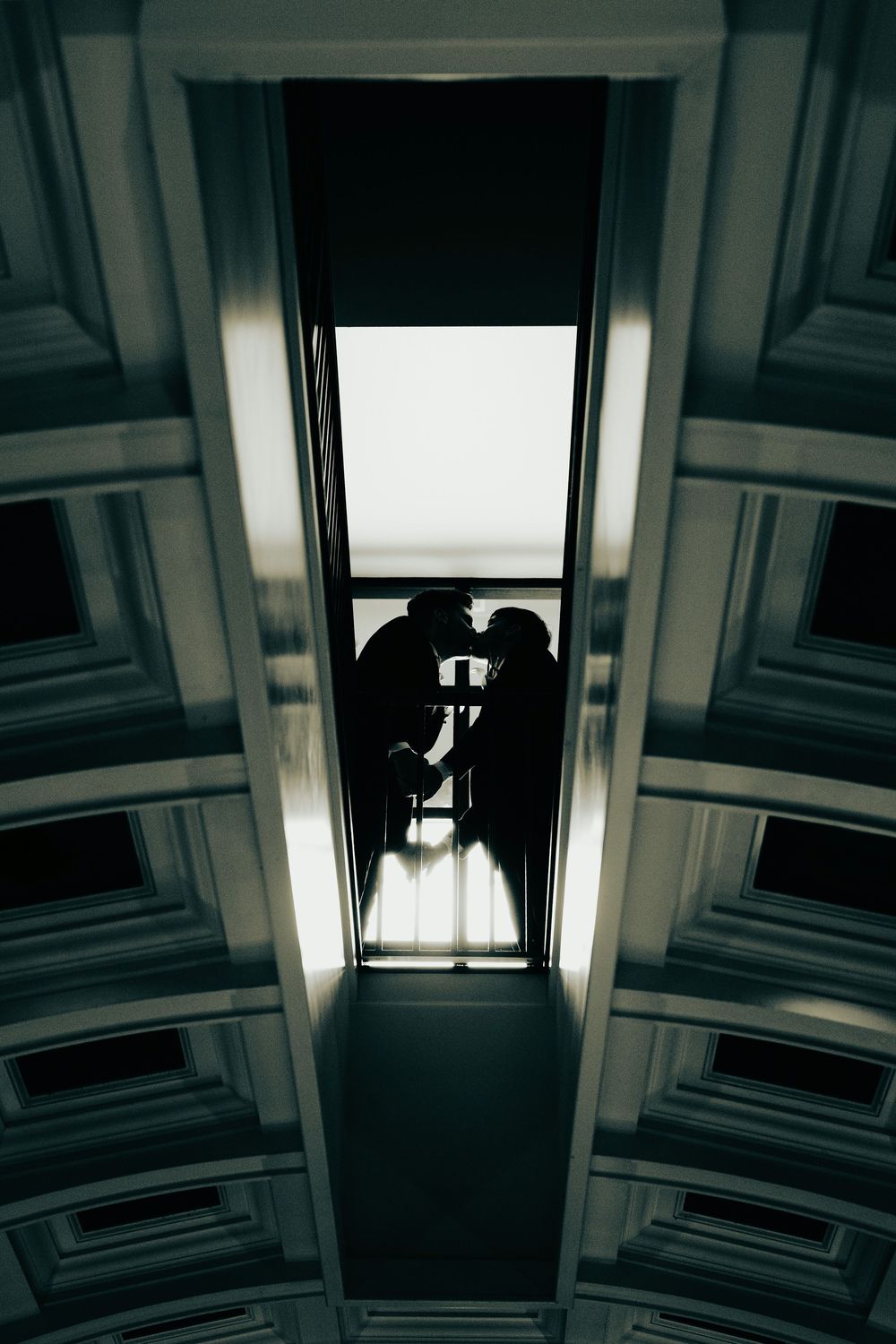 Silhouette of couple kissing in a doorway, viewed from below through an ornate architectural ceiling frame.