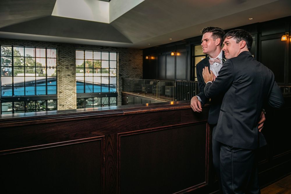 Two men in suits share an intimate moment overlooking an indoor pool at an elegant venue.