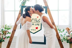 Wedding ceremony scene in bright white indoor venue with wooden beams and large windows.