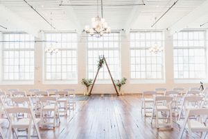 A minimalist white wedding venue with wooden floors, white chairs, and elegant chandeliers.