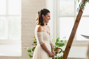 Intimate wedding ceremony moment in bright white room with wooden arch and greenery.