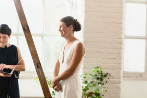 A white wedding dress being fitted in a bright indoor space with brick walls.
