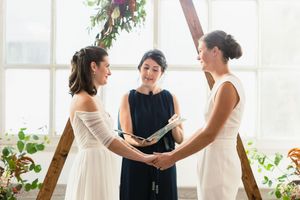 Wedding ceremony preparations in bright sunlit room with wooden arch and white walls.
