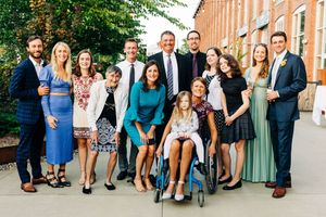 Large wedding party group photo outside brick building in formal attire.
