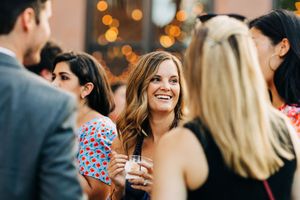 Wedding reception guests mingling and laughing in dimly lit venue with warm lighting.