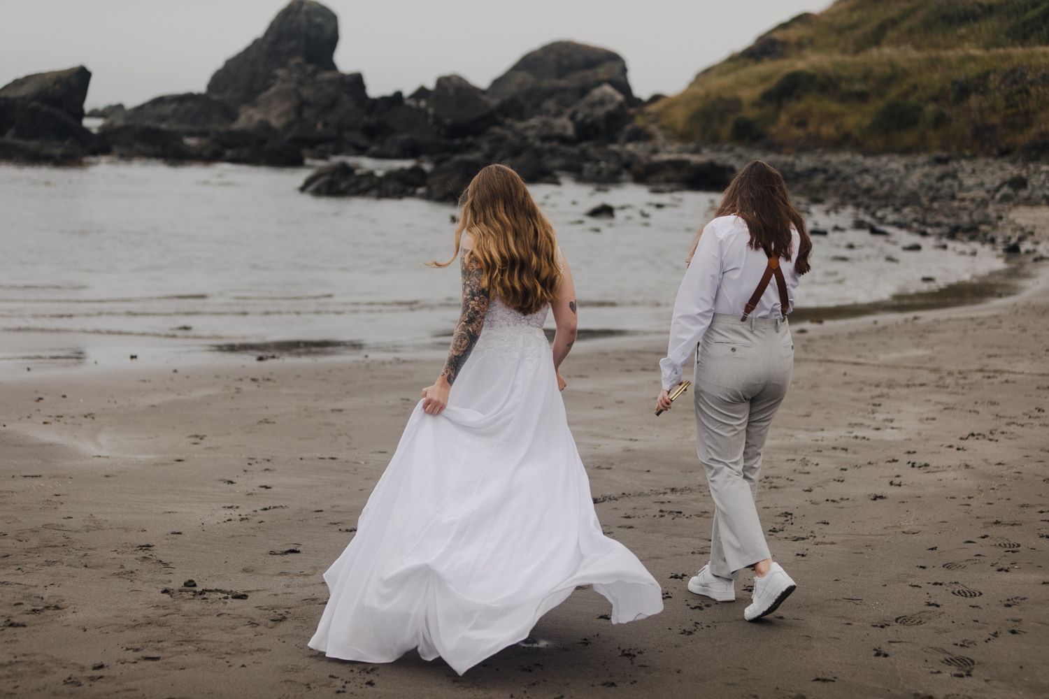 Lesbian couple walks on the rocky beach of the southern Oregon Coast before their elopement ceremony