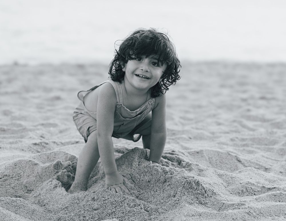 Young girl with curly hair smiling and playing in the sand at the beach.