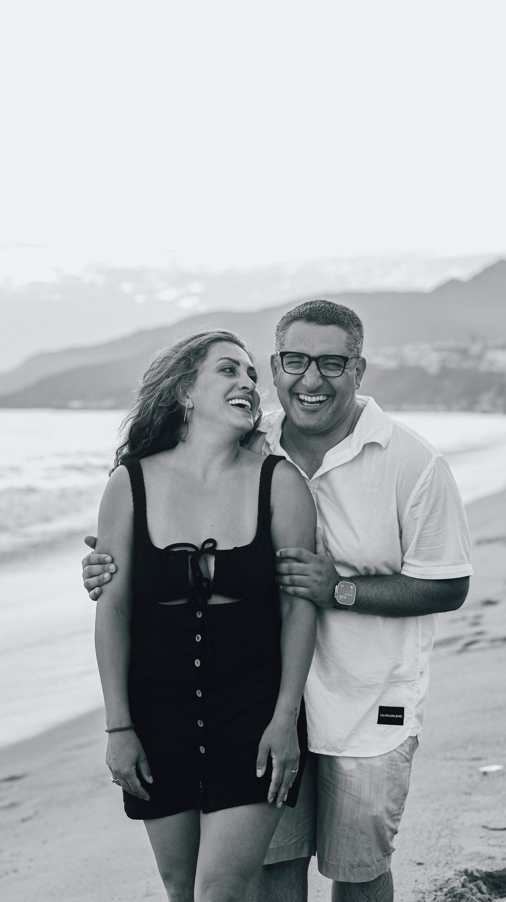 Happy couple embracing and smiling on a beach in black and white photo.