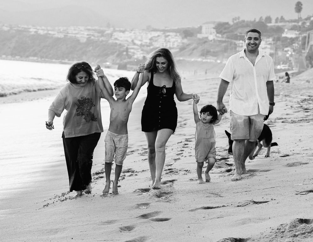Black and white photo of a happy family walking on a beach, holding hands with children and a dog.