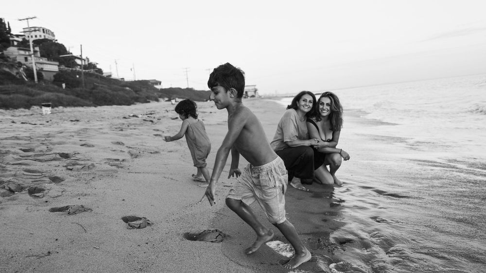 Children and women enjoying a sunny day on a sandy beach in a black and white coastal photograph.
