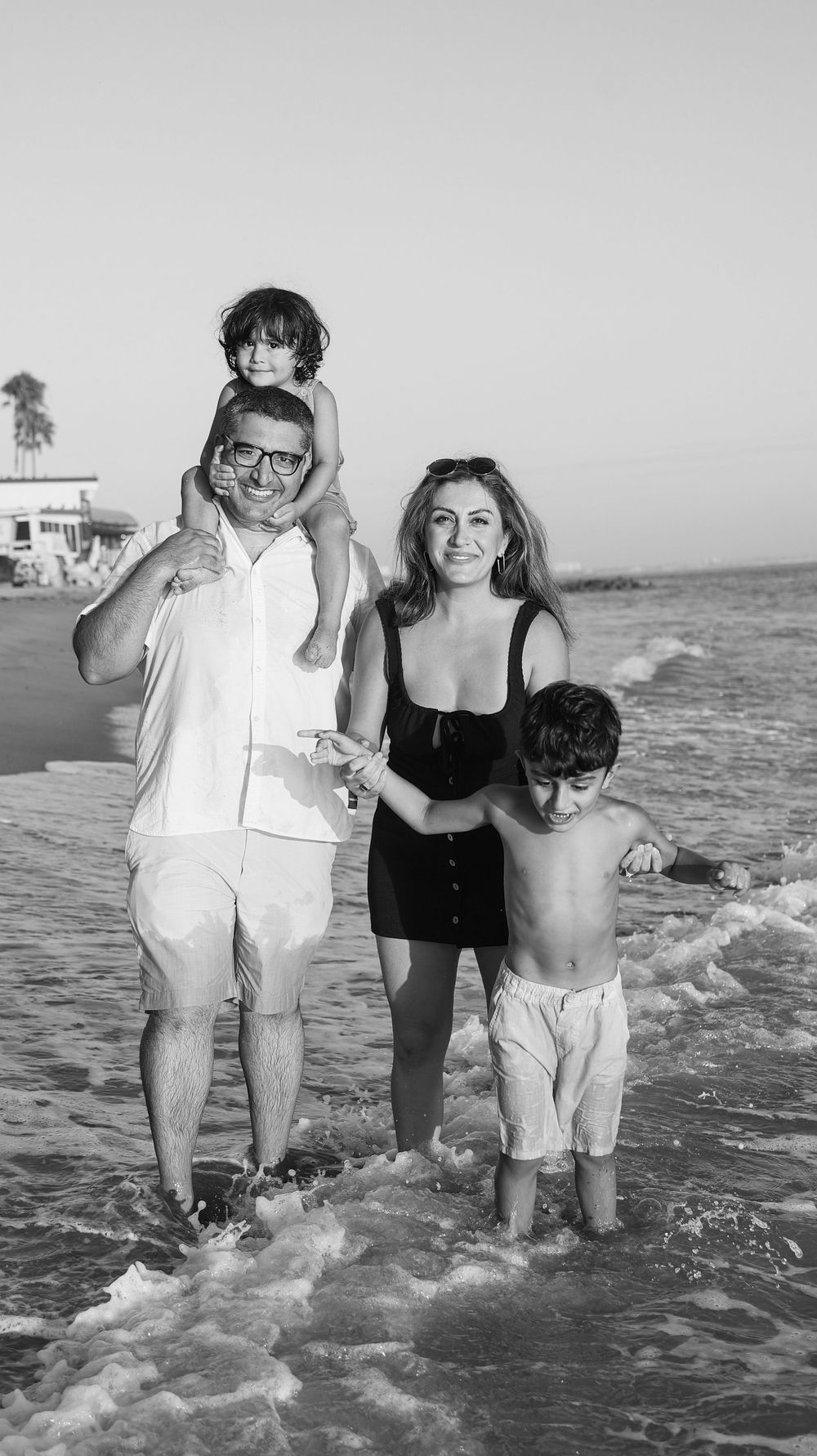 Family of four enjoying beach waves, black and white photo with parents and two young children.