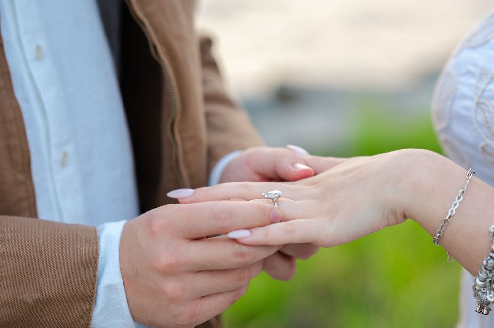 Close-up of a man placing a diamond engagement ring on a woman's finger during a romantic proposal.
