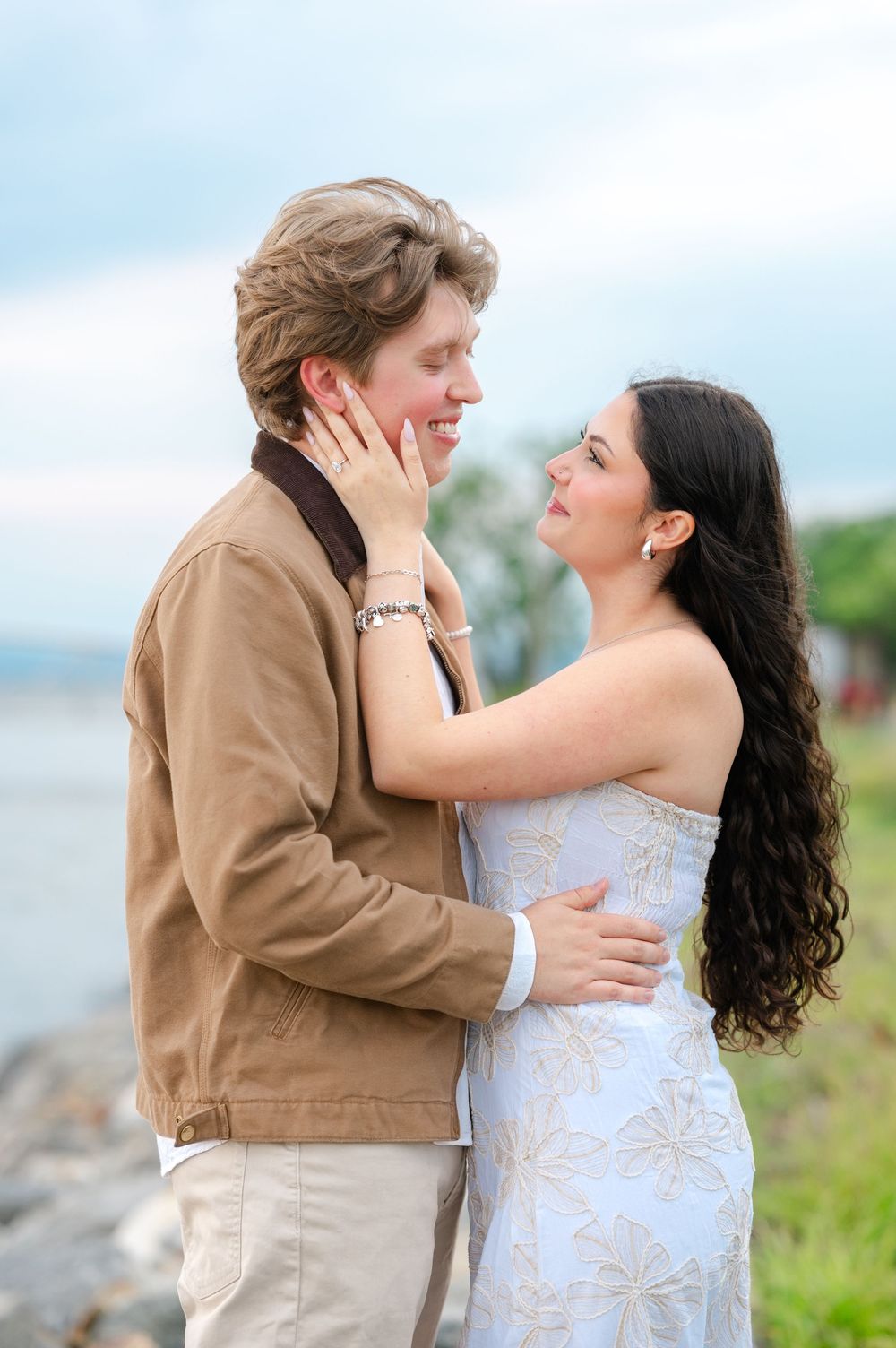 Happy couple embracing and smiling at each other near rocky waterfront.