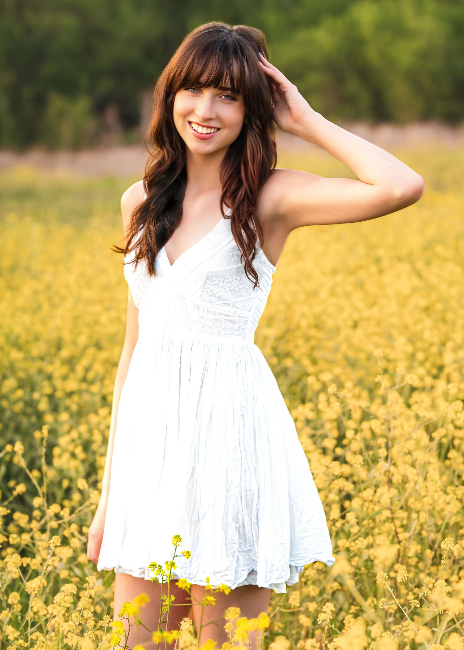 Young woman in white dress poses among sunflowers in a field, with a yellow flower tucked in her hair.