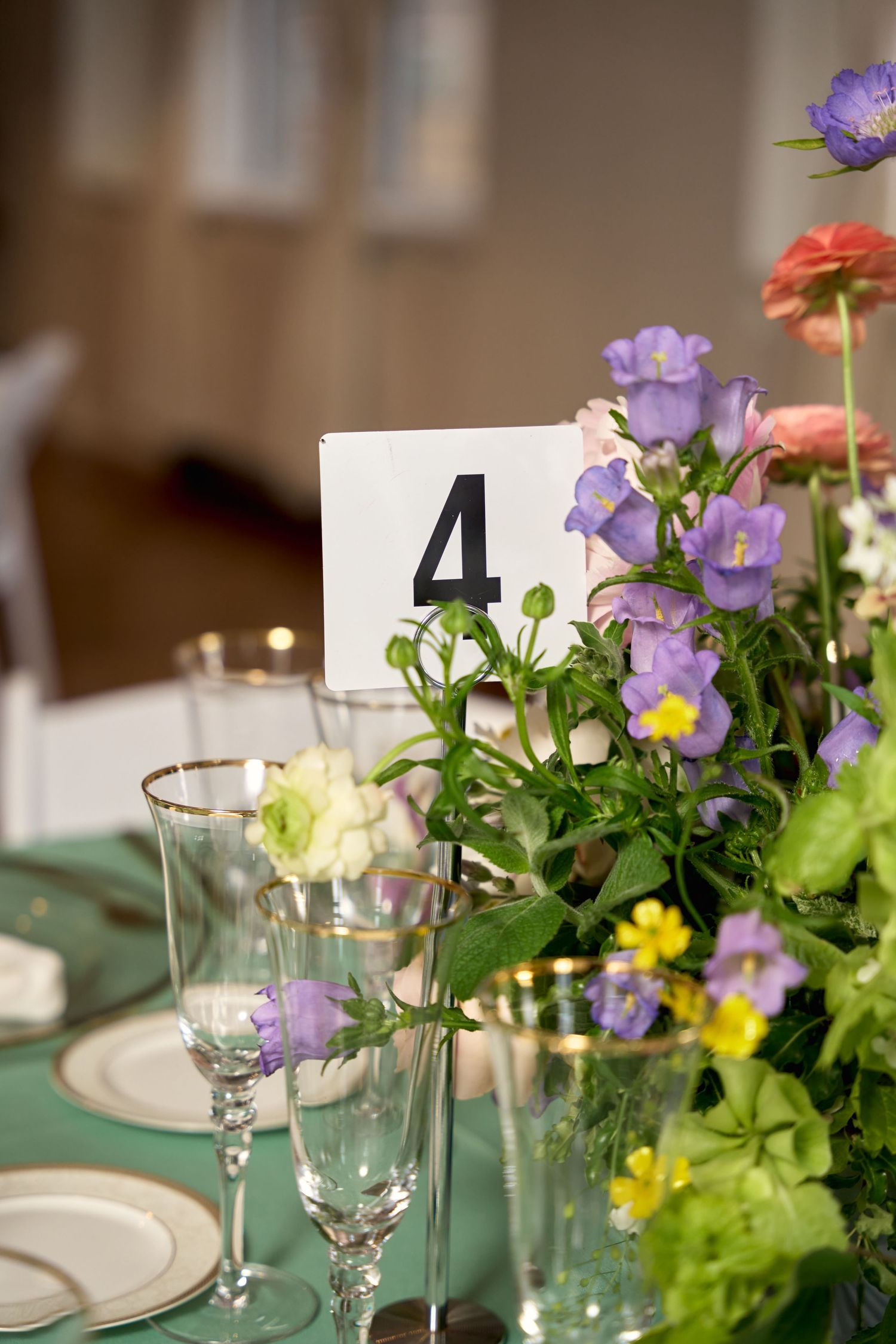 Elegant wedding table 4 setting with purple and pink floral centerpiece on green tablecloth with crystal glassware.