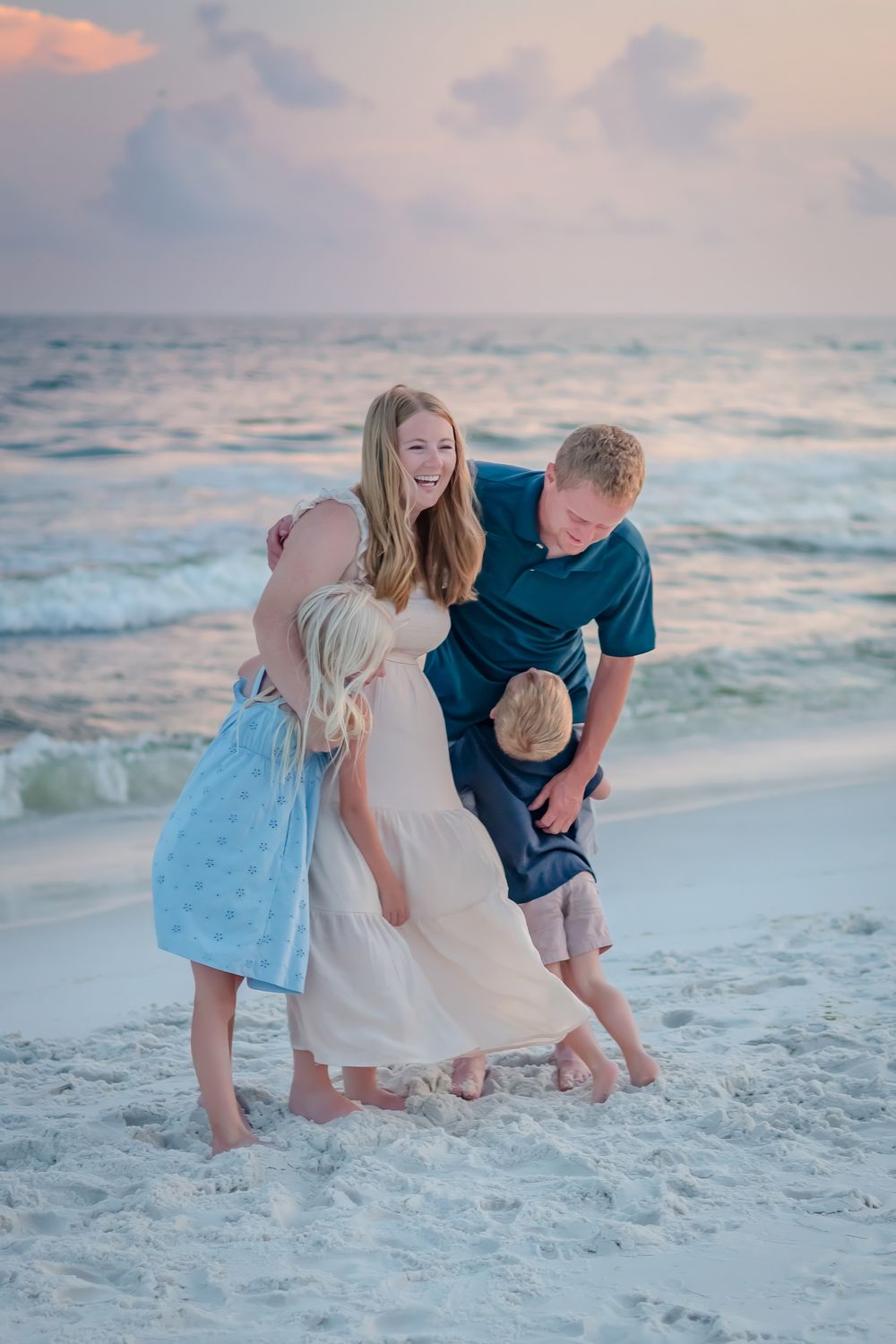 Happy family of four laughing and playing together in the ocean waves at sunset on the beach.