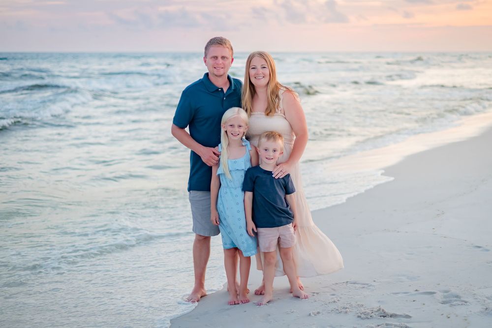 Family of four posing together on a beautiful beach at sunset with turquoise ocean waves behind them.