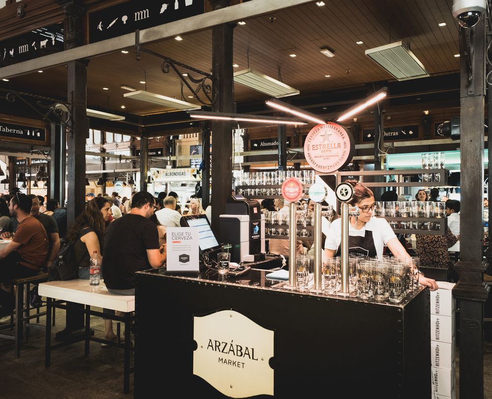 Arzabal Market bar inside Mercado de San Miguel Madrid with beer taps, bartender serving customers in busy market.