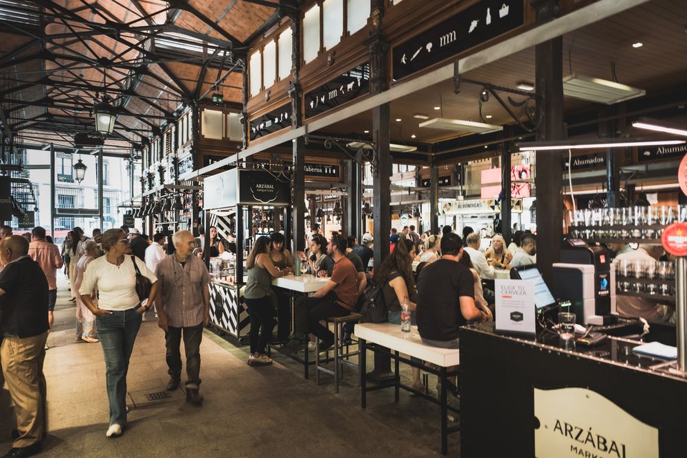 Lively Mercado de San Miguel in Madrid with Arzabal bar, dining patrons, and vendors in historic iron market hall.