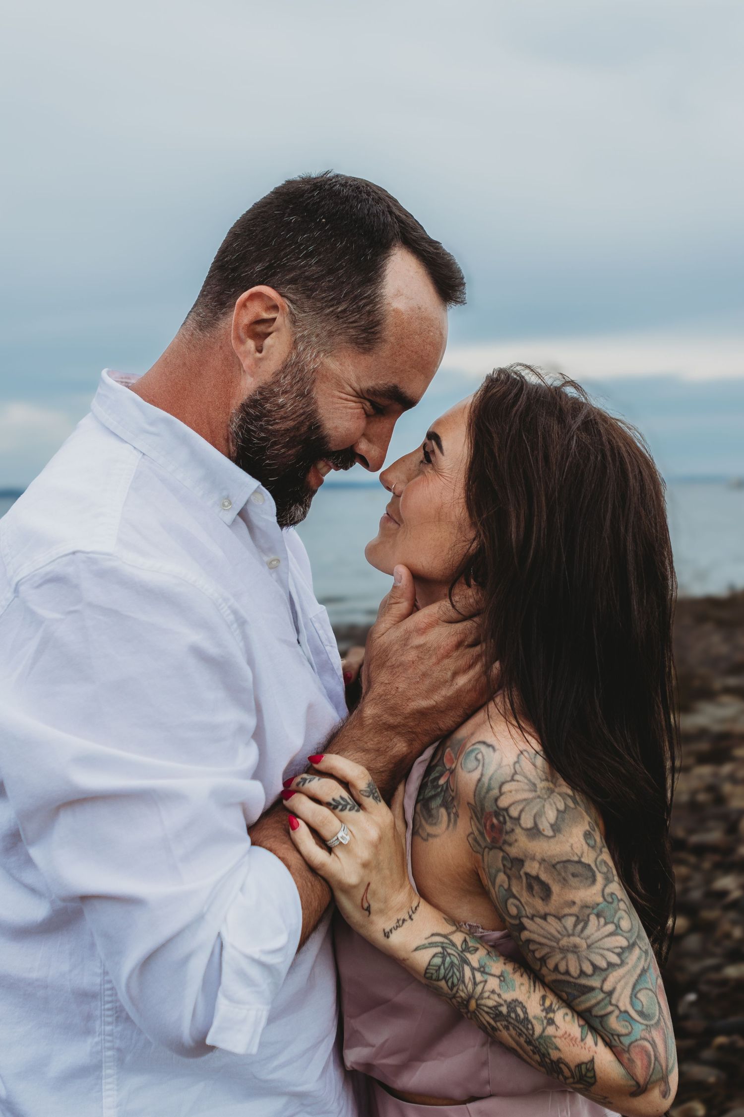 Couple kissing on beach holding a floral Save the Date chalkboard sign for 7-17-2021.