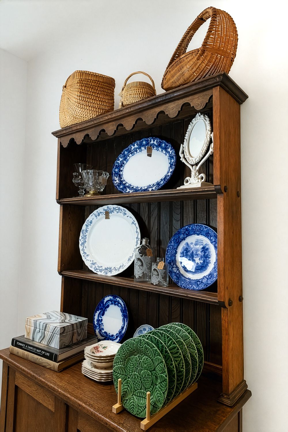 Antique wooden hutch displaying blue and white china plates, wicker baskets, and green cabbage leaf plates on shelves. Swell House La Grange