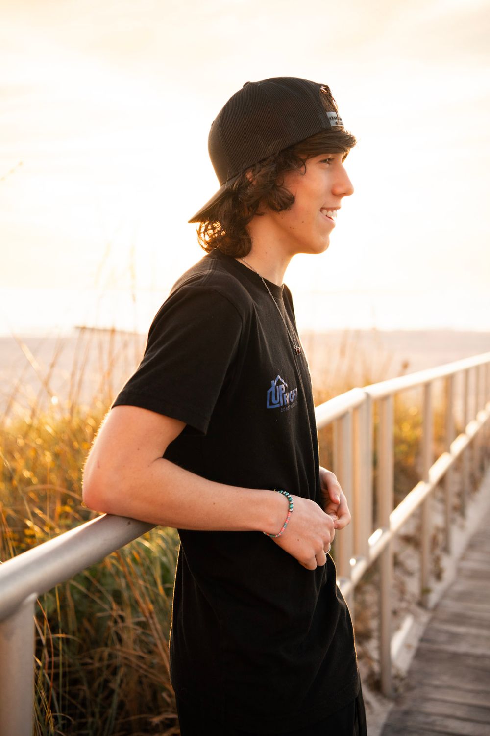 High school senior leaning against a boardwalk railing during a sunset portrait session at Madeira Beach, Florida.