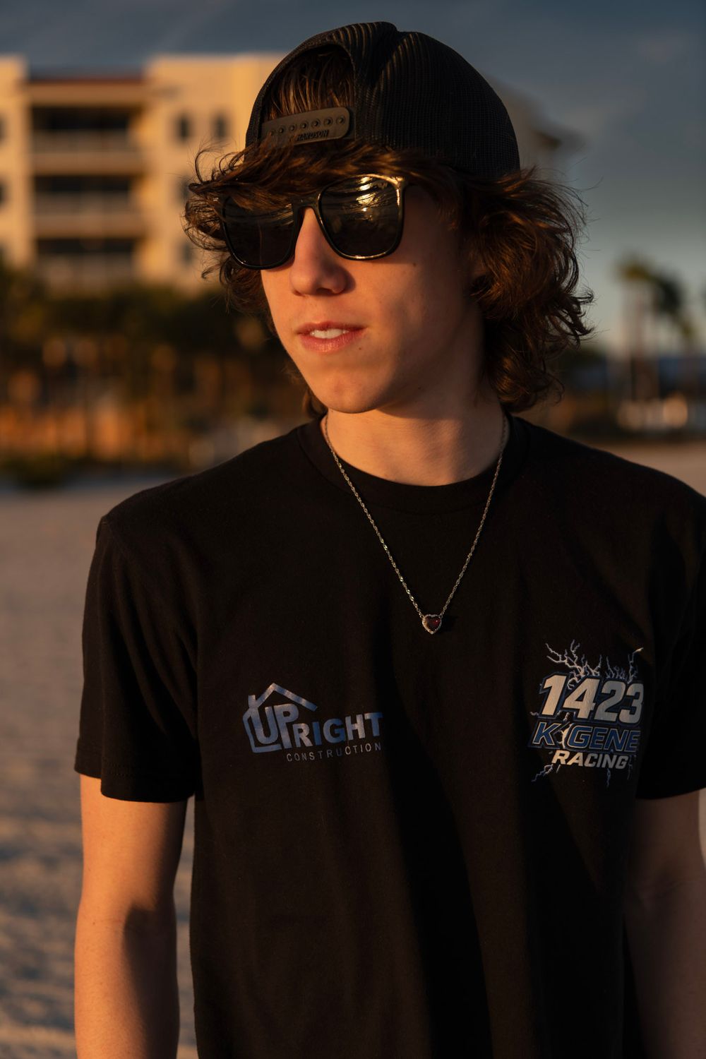 Senior boy wearing sunglasses and a black hat posing on Madeira Beach during golden hour.