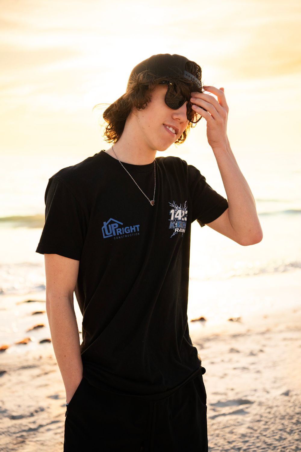 Smiling high school senior standing on the shoreline at Madeira Beach with the sun setting behind him.