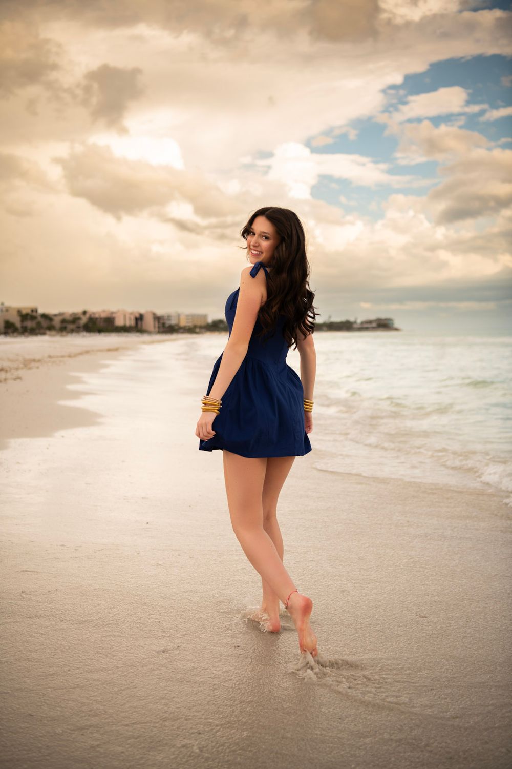 Senior portrait of high school graduate walking barefoot along Clearwater Beach shoreline at sunset.
