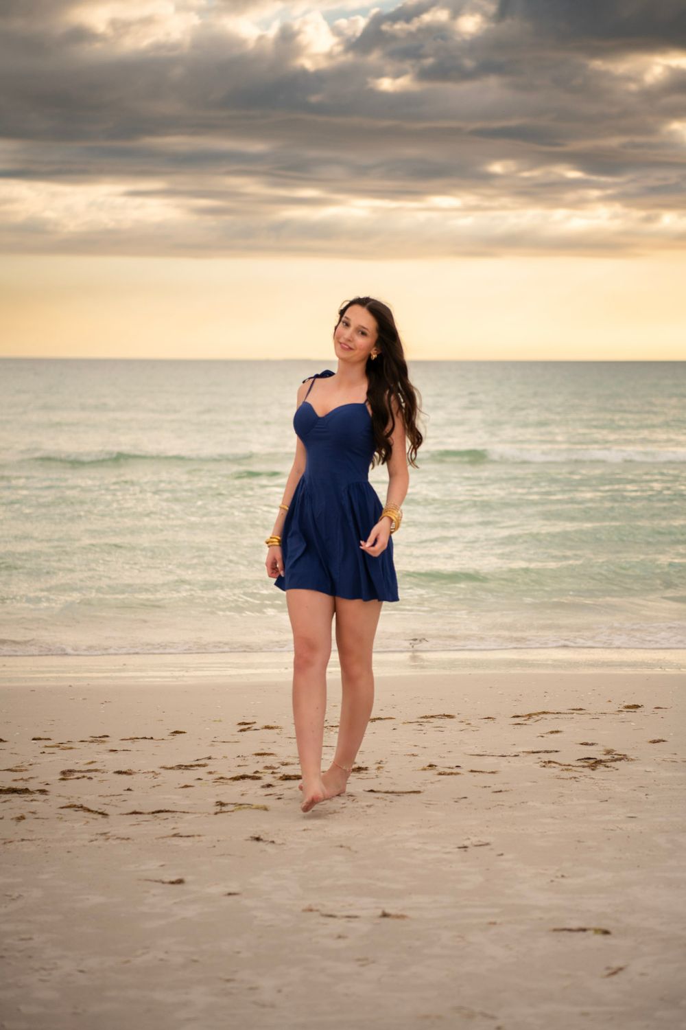 Full-length senior photo of graduate standing on Clearwater Beach during golden hour.