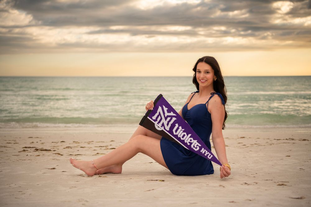 High school senior sitting on Clearwater Beach holding graduation stole during sunset portrait session.