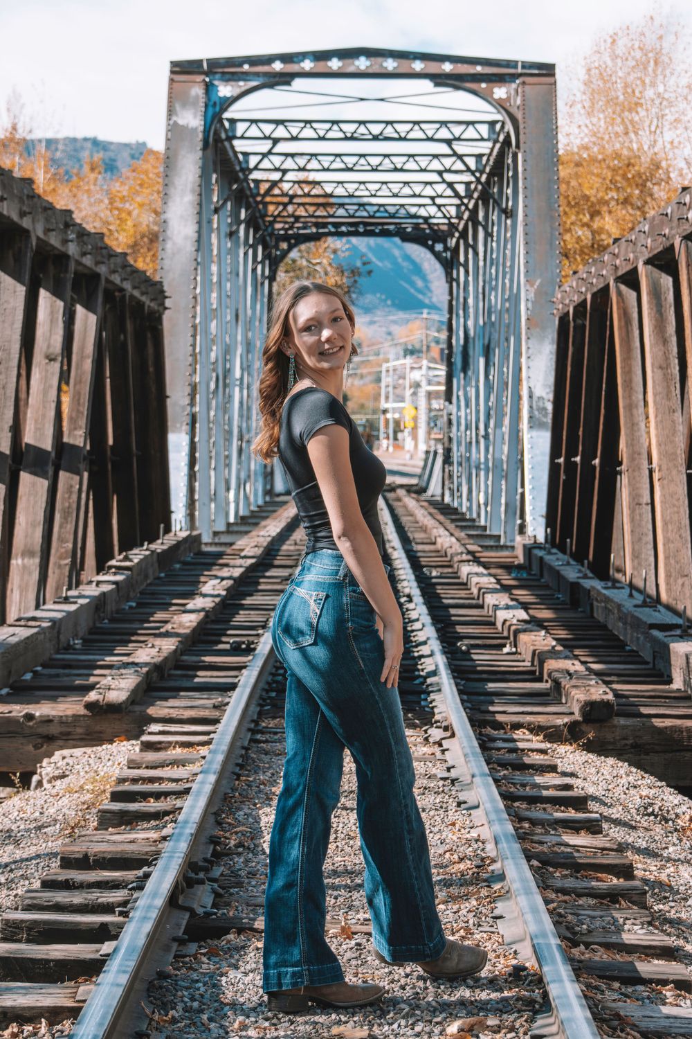 Standing on railroad tracks inside a metal bridge structure with mountains in background.