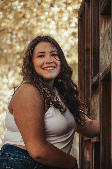Rustic outdoor portrait with warm golden bokeh and wooden architectural elements.