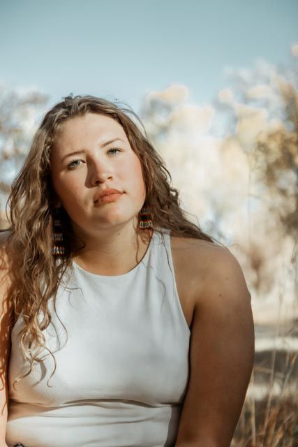 Outdoor portrait against soft bokeh background with warm golden lighting and natural styling.