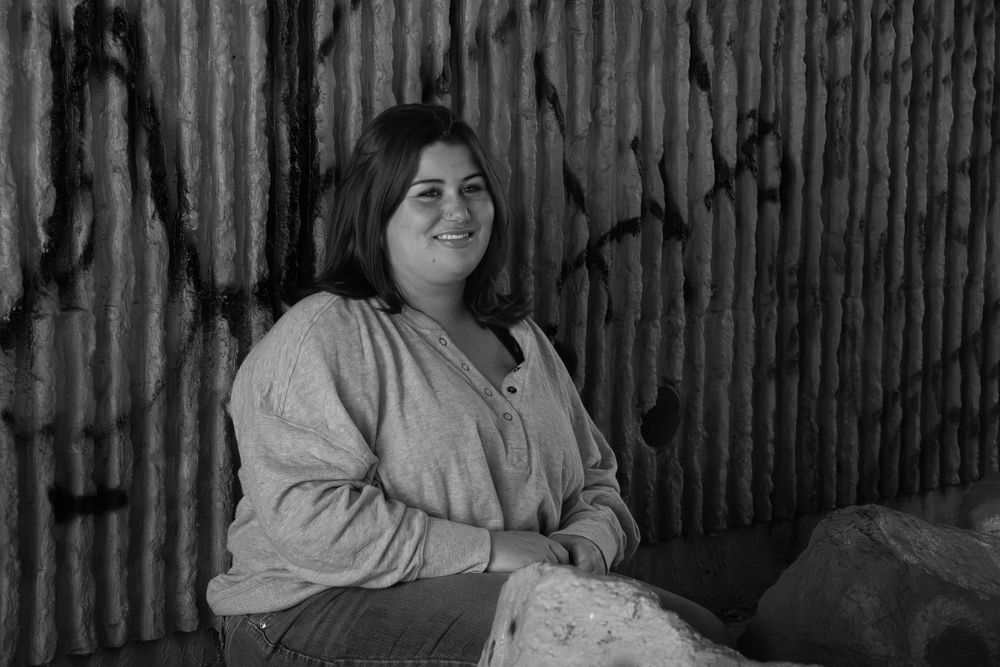 A black and white photograph shows a group of people sitting together and smiling in a casual outdoor setting.