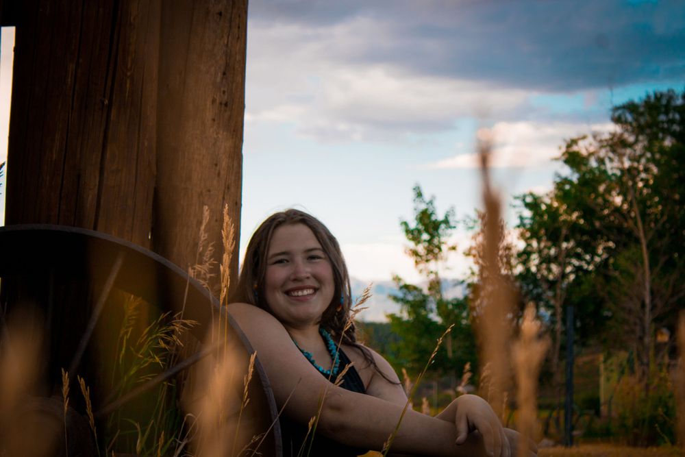 Outdoor portrait in golden evening light with rustic wooden post and natural bokeh background.